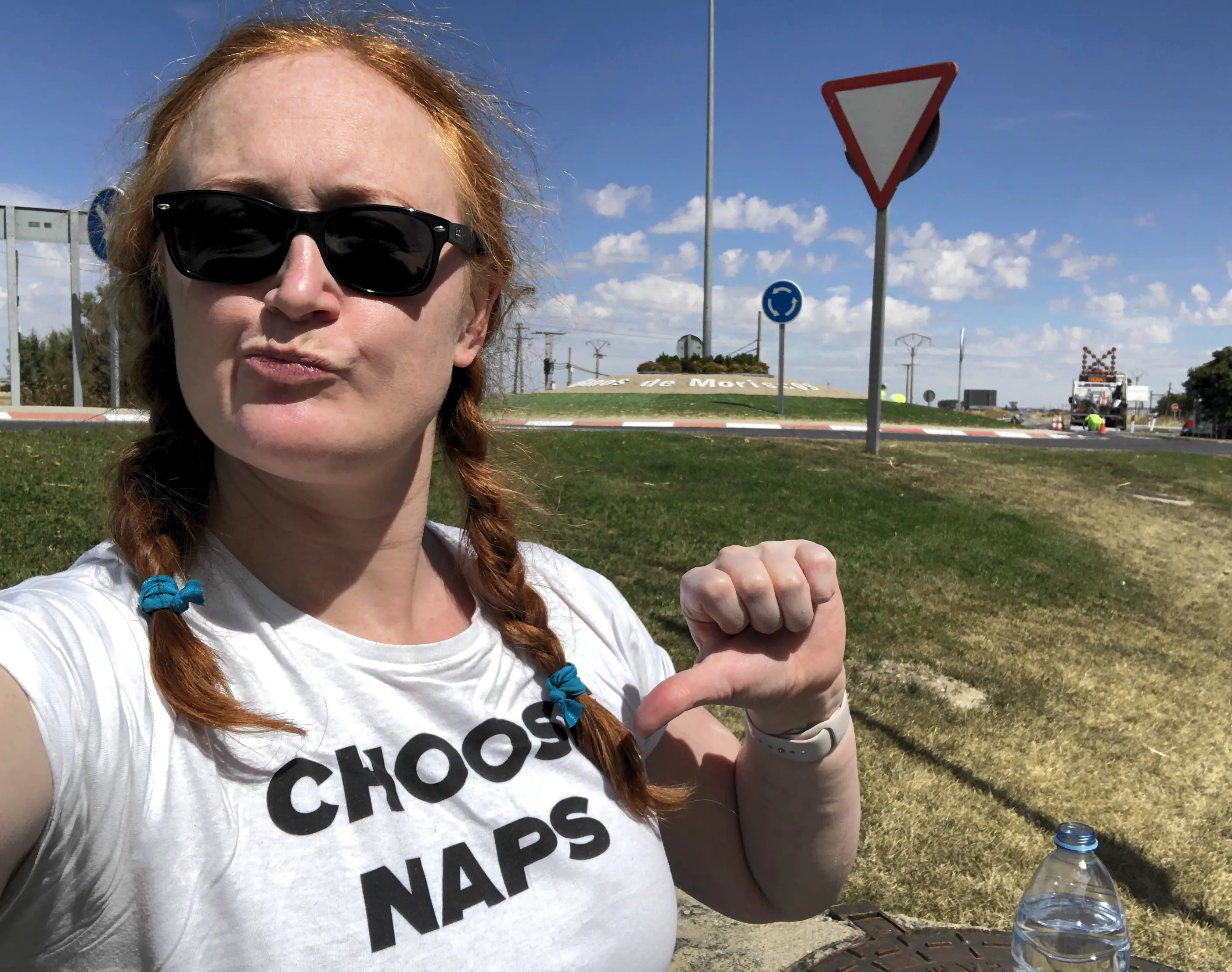 Sarah (a red-headed woman) sitting in the sunshine, pointing at a shirt that reads Choose Naps.